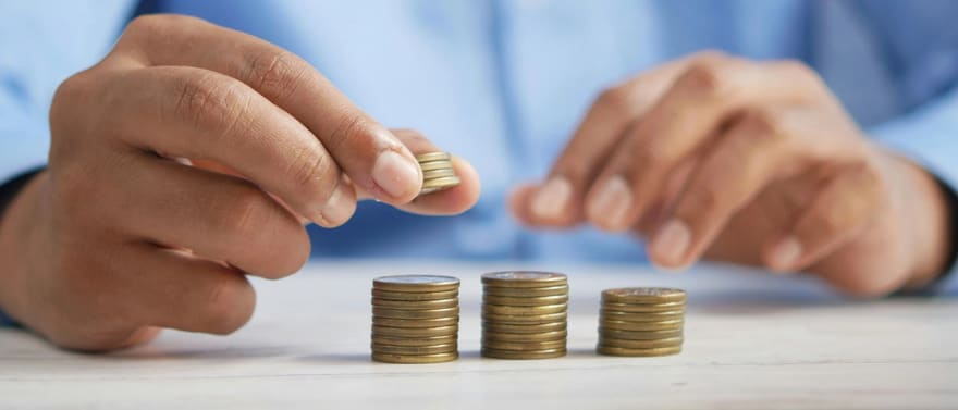 Mãos empilhando moedas em três pilhas sobre uma mesa.
