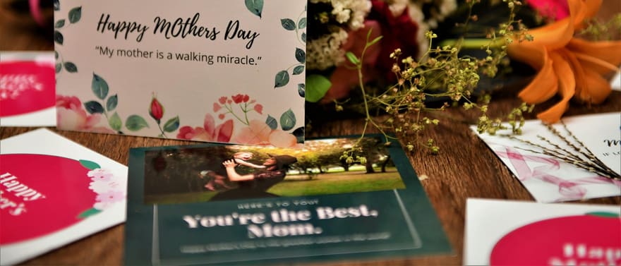 Cartões de Dia das Mães entre flores sobre uma mesa.