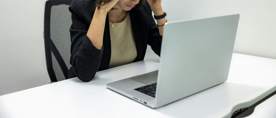 Mulher com as mãos na cabeça, com expressão preocupada, diante de um notebook.