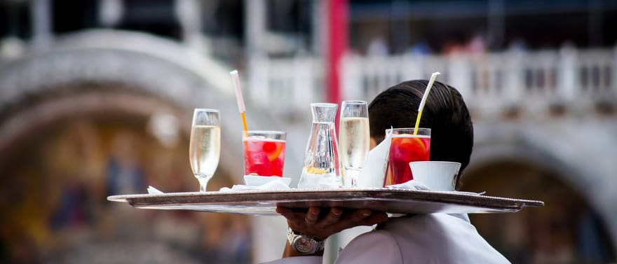 Garçom carregando uma bandeja com taças de bebidas.