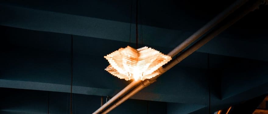 Salão de restaurante à meia-luz, com luminárias pendentes e cadeiras laranja.