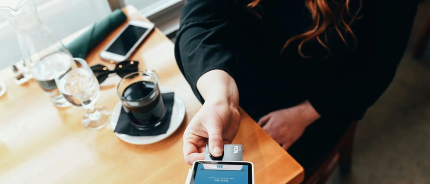Cliente aproximando o cartão de uma maquininha de pagamento em uma mesa de café.