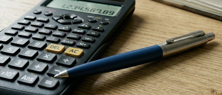 Calculadora científica e caneta sobre uma mesa de madeira.