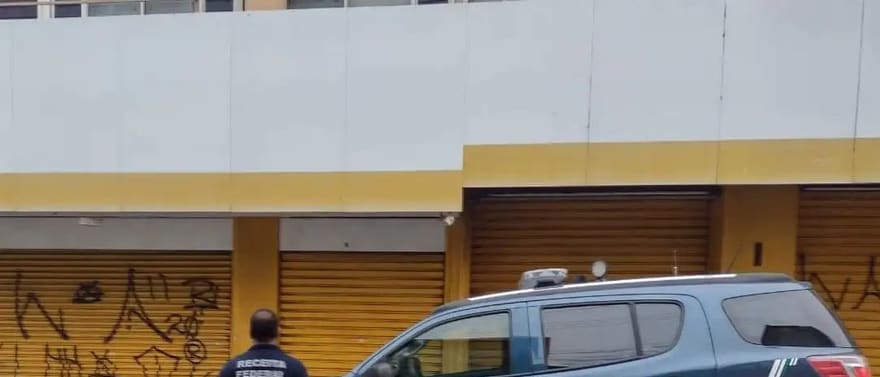 Agente ao lado de uma viatura da Receita Federal estacionada em frente a portas de aço.