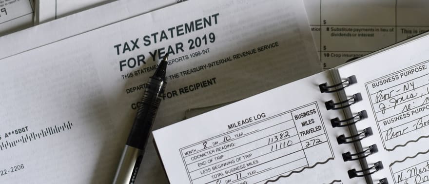 Formulários fiscais (“Tax Statement for year 2019”) e um caderno de registro com caneta.