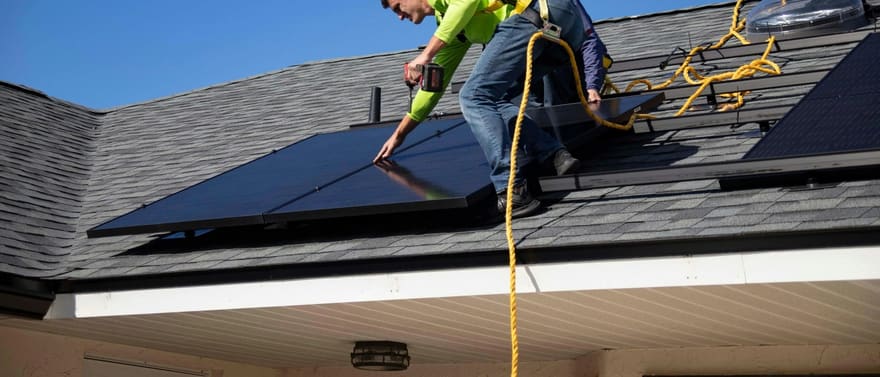 Instalador fixando painéis solares no telhado de uma casa.