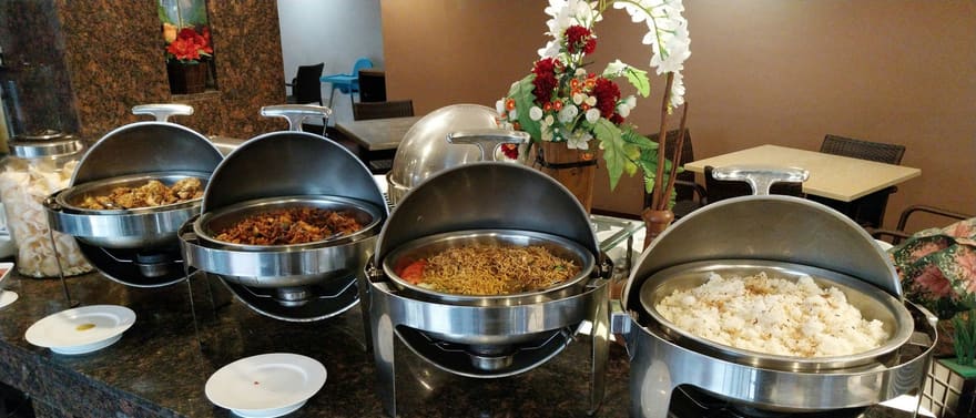 Réchauds de bufê com comida e pratos brancos sobre um balcão.