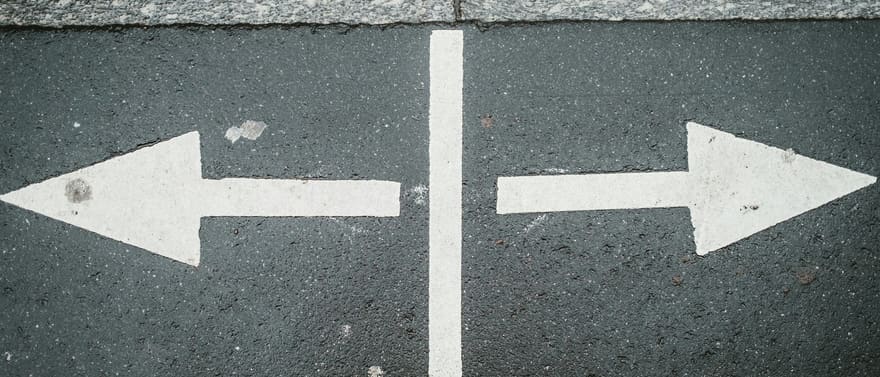 Duas setas brancas pintadas no asfalto, apontando em direções opostas e separadas por uma faixa vertical.